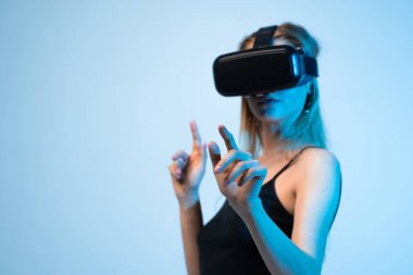 VR kulaklık takan ve sanal bir çevreyle etkileşim halinde olan bir kadının yan görüş portresi. Büyüleyici teknoloji ve dijital kullanıcı arayüzü kavramı.