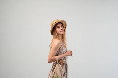 Tekrar kullanılabilir bir ağ torbasını elinde tutan genç bir kadının yandan görünüşü. Sürdürülebilir yaşam tarzı, eko-alışveriş, asgari moda, sıfır atık ve bilinçli tüketim kavramı.