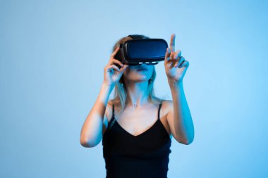 Kadın oyuncu sanal bir çevreyi iki elini de kullanarak keşfeder ve bir VR kulaklık takar. Futuristik oyun, el takibi, sürükleyici deneyim, dijital etkileşim ve gelecek nesil eğlence..