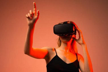 Sanal gerçeklik kulaklığı takan kadın oyuncu el hareketleriyle dijital oyun ortamıyla etkileşime giriyor. Kapsamlı oyun kavramı, gelecekteki eğlence, VR teknolojisi ve etkileşim.