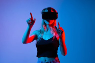 VR kulaklık takan ve dijital arayüzü el hareketleriyle kontrol eden bir kadının gelecekteki sanal etkileşim konsepti. Etkileyici teknoloji teması yenilikçilik, metaevren kullanımı ve dijital iletişim üzerine odaklandı.