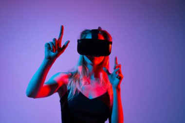 Sanal gerçeklik oyun oturumunda VR kulaklığını ayarlayan kadın oyuncu. Fütürist neon kırmızı ve mavi stüdyo ışıklandırmalı büyüleyici VR oyun deneyimi kavramı.