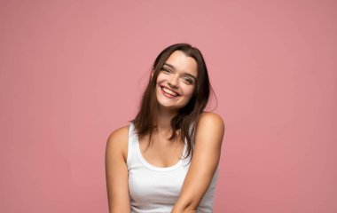 Kafasını pembe arka plana yaslayan kahverengi saçlı ve yumuşak gülüşlü genç bir kadının portresi. Arkadaşça ifadesi sıcaklığı, ulaşılabilirliği, güveni ve insani duyguları ifade ediyor..