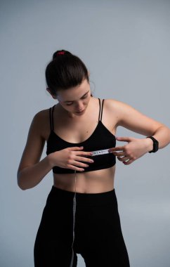 Sportif kadın, mezura kullanarak vücut ölçülerini dikkatlice kontrol ediyor. Sağlık izleme, zindelik değerlendirmesi, sağlıklı rutin ve modern stüdyo yaşam tarzı tasviri kavramı.