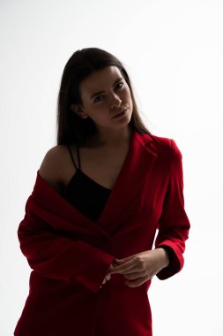 Kırmızı ceketli zarif bir kadın stüdyoda sakin ve düşünceli bir ifadeyle poz veriyor. Özgüven, denge ve çağdaş stili vurgulayan minimal moda portresi.