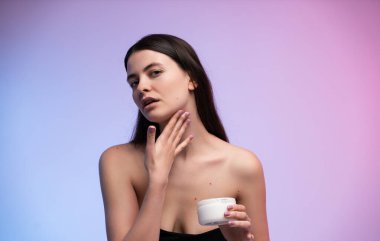 Elinde kozmetik kavanozu tutarken boynuna nazikçe masaj yapan genç bir kadının portresi. Pastel gradyan arka plan temiz güzellik, cilt bakımı ve sağIık kavramını iletir.