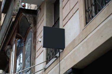 Eski bir taş bina cephesinden yansıyan boş dikdörtgen karanlık tabela, özel marka ya da reklam için hazır, süslü bir pencerenin bulanık arka planı ve işlenmiş demir balkon