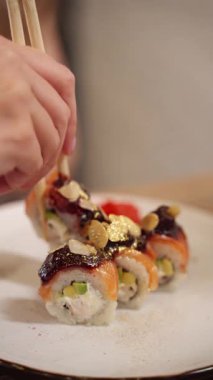 Lezzetli bir gurme suşi yerken, yemek çubuklarıyla altın yapraklı bir soya balığı alıp soya sosuna batıran birinin yakın çekimi.