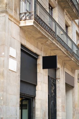Boş bir siyah açık hava tabelasını sergileyen taş bina, perakende markalaşma için ideal, kapalı mağazalar, dekoratif balkonlar ve şehir ortamında işlenmiş demir parmaklıklar.