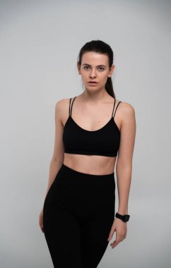 Minimum siyah spor sutyen ve bileğinde akıllı bir taytla genç bir kadın basit bir arka plana karşı duruyor spor kıyafetleri, modern spor giyim ve aktif yaşam kavramları somutlaştırıyor.