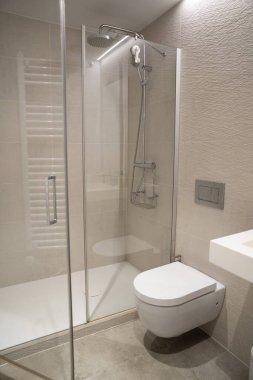 Cam duş kabini olan modern banyo, duş başlığı ve duvara monte edilmiş tuvalet, tarafsız kiremitlerde temiz minimalist tasarım sergileniyor, yeni inşaatlar veya gayrimenkul listeleri