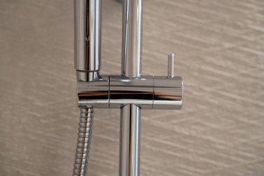 Çağdaş bir banyoda modern tasarım ve işlevselliği, temiz metalik detaylarla sergileyen kaygan demiryolu üzerinde esnek hortumu olan krom duş başlığı.