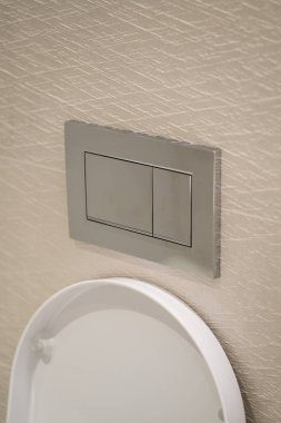 Krom sifonu çekme düğmesi beyaz bir tuvaletin üstündeki desenli duvar paneline kurulmuş, su koruma ve modern banyo teknolojisini verimli bir temizlik için gösteriyor.