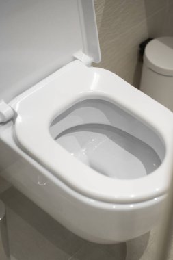 Çağdaş bir banyo ortamında açık koltuk kılıfı olan beyaz seramik klozet, parlak ışığı yansıtıyor ve modern tasarım, hijyen ve temiz tesisat donanımlarını vurguluyor.