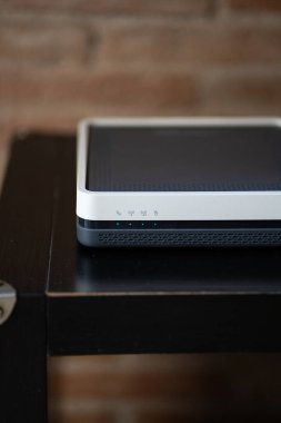 Koyu ahşap bir masa üzerinde parlayan mavi gösterge ışıklarına sahip modern kablosuz modem internet bağlantısını, ev ağını ve dijital iletişim teknolojisini sembolize ediyor.