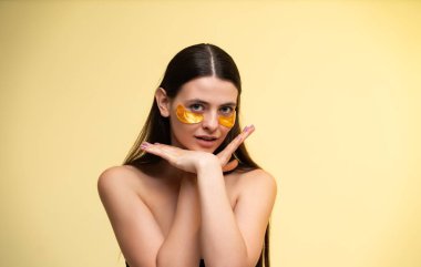 Genç bir kadın altın göz bandı uyguluyor, kendine özen gösteriyor ve cildini sulandırıyor, sağlığını ve parlayan tenini odaklanmış bir ifadeyle destekliyor.