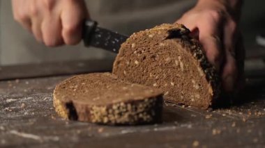 Fırıncıların elleri, un kaplı, rustik ahşap bir masada bir somun taze, kabuklu tam tahıllı çavdar ekmeğini dilimliyor.