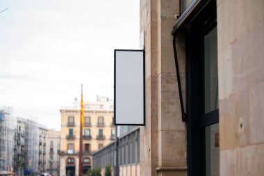 Boş dikey tabela bej taş cephe üzerine monte edilmiş, reklam veya markalaşma için temiz kopya alanı sunan, yumuşak bulanık şehir caddesi ve mağaza önü karşı kurulmuş