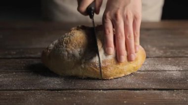 Fırıncının elleri, yeni pişmiş ekmek dilimlemek için bıçakla un kaplı, ahşap bir masanın üzerinde.