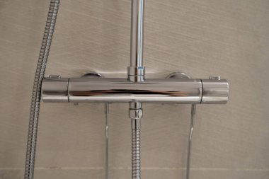 Krom termostatik duş karıştırıcı, el yapımı sprey hortum ve açık gri fayanslı banyo duvarına yerleştirilmiş eşyalar. Banyo için çağdaş tasarım ve işlevsellik sunuyor.