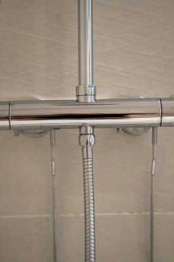 Modern krom duş karıştırıcı musluğu, esnek bir hortum ve açık bej desenli fayansların dikey boru tamiri çağdaş banyo tasarımı ve tesisat kurulumunu temsil ediyor.