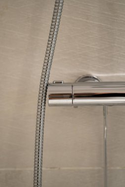 Modern krom termostat duş karıştırıcısı su sıcaklığını düzenliyor, esnek bir hortumla bağlanıyor, iç banyo ortamındaki pürüzsüz metal bitiş ve fonksiyonel tasarımı vurguluyor.