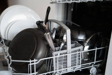 Kirli tabaklar, yemek takımları ve çatal bıçaklarla dolu bulaşık makinası. Yıkanmaya hazır. Temizlikten sonra, ev işlerini ve mutfak aletlerini renklendiriyor.