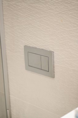 Çağdaş tuvaletlerde su verimliliğini ve sürdürülebilirliği teşvik eden, desenli bej bir duvara monte edilmiş iki metalik dikdörtgen sifon plakalı modern sifon düğmesi.