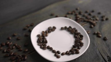 Erkek el, siyah bir masada kalp şeklinde kavrulmuş fasulyelerle süslenmiş çay tabağına beyaz, sıcak, siyah bir kahve koyuyor.