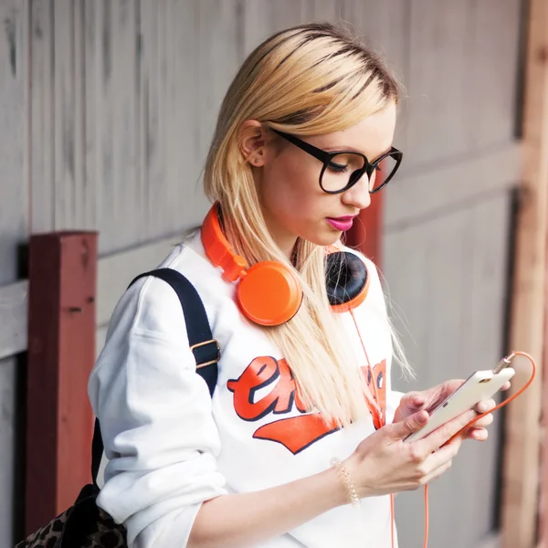 Meisje met oranje koptelefoon op zoek naar geweldige track in haar telefoon. Straat schieten, muziek energie, lifestyle, Europese of Amerikaanse stijl, helder geluid, zonneschijn, outdoors — Stockfoto