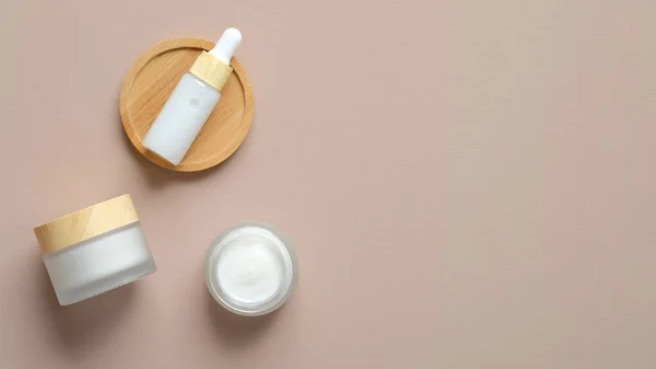 Set of natural cosmetic products on beige background. Flat lay serum dropper bottle and moisturizer cream jars. Organic beauty products top view.