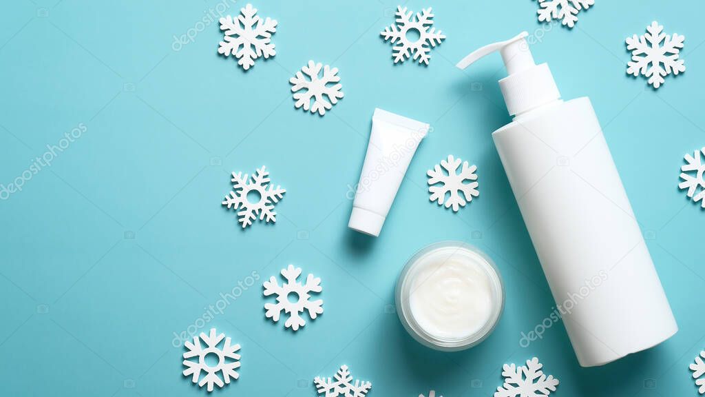 Winter skin care cosmetic products on blue background with snowflakes. Beauty products packaging design template. Moisturizer cream jar, pump bottle, tube.