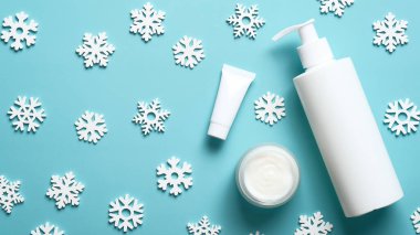 Kış Cilt Bakımı Kozmetikleri. Beyaz boş pompa şişesi, kavanoz ya da nemlendirici krem, tüp ve yapıştırıcı mavi arka planda kar taneleri. Düz yatış, üst görünüm.