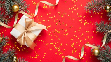 Altın kurdeleli hediye kutusu, parlak konfeti, kırmızı arka planda altın topları olan Noel ağacı dalları. Noel ya da yeni yıl konsepti. Düz yatış, üst görünüm.