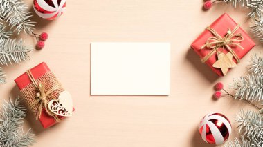 Boş kağıt kart ve el yapımı Noel süslemeleri, kırmızı hediye kutuları, pastel bej arka planda toplar. Düz konum, üst görünüm, kopyalama alanı. Noel tebrik kartı maketi.