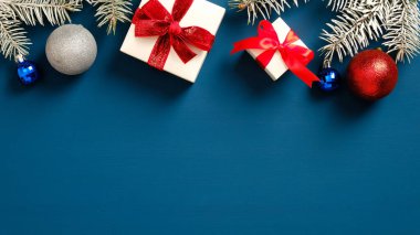Hediye kutularından ve koyu mavi arka planda topları olan çam dallarından oluşan bir Noel çerçevesi. Düz yerde, üst tarafta. Noel kartı şablonu, yeni yıl afişi modeli.