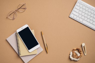Klavyesi, akıllı telefonu, kağıt defterleri, kahverengi arka planda kadın aksesuarları olan modern kadın çalışma alanı. Serbest ofis masası. İş konsepti.