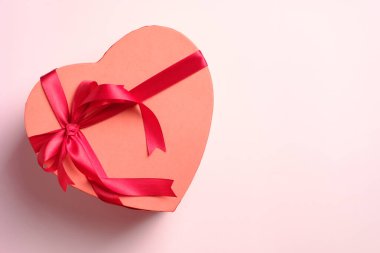 Pembe arka planda kırmızı kurdeleli kalp şeklinde bir kutu. Sevgililer günün kutlu olsun tebrik kartı şablonu.
