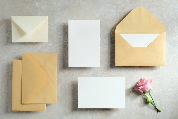 Wedding stationery mockups. Flat lay blank paper card, envelopes, flowers on concrete table. Top view.