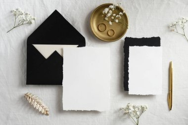 Zarif düğün kırtasiyesi üst görünümü. Düz yatıyordu boş davetiye maketleri, altın süslemeler, pastel beyaz arka planda çingene çiçekleri.