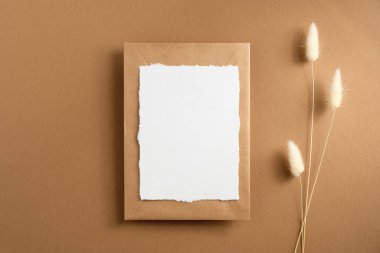 Düğün davetiyesi ve kahverengi arka planda kurumuş çiçeklerle birlikte zarf modeli. Düz yatış, üst görünüm.