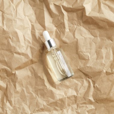 Kraft kağıt üst görüşünde şeffaf serum şişesi. Cilt bakımı için doğal yağ içeren damperli konteynır.