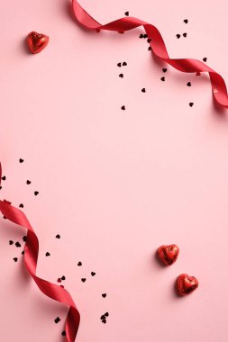 Kırmızı kurdeleli, konfetili, pembe arka planda kalp şeklinde şekerlemeleri olan zarif sevgililer günü geçmişi. Asgari düzeyde. Düz yatıyordu.