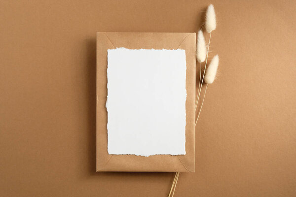 Пустая бумажная карточка и бумажный конверт с сушеными цветами на коричневом фоне. Плоский, вид сверху.