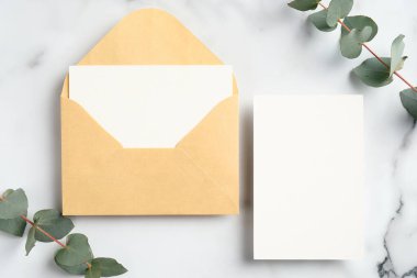 Üst düzey düğün davetiyeleri ve okaliptüs yaprakları mermer masada. Düğün kırtasiyesi seti.