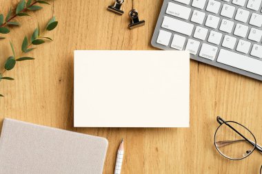 Klavyeli, okaliptüs yapraklı, gözlüklü, ahşap ofis masasındaki boş kağıt kart. Düz yatış, üst görünüm.