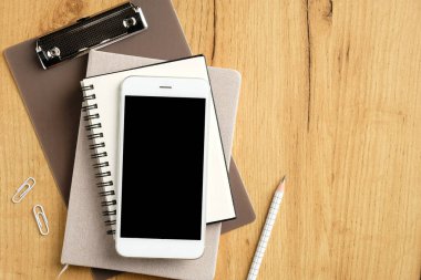 Bir yığın kağıt defter, pano ve ahşap ofis masasında akıllı telefon. Düz yatış, üst görünüm.