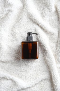Kehribar cam şampuan şişesi beyaz havluda. Düz yatış, üst görünüm.