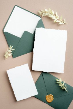 Düğün detayları, düğün zarfları, pastel bej arka planda kurumuş çiçekli düğün davetiyeleri..