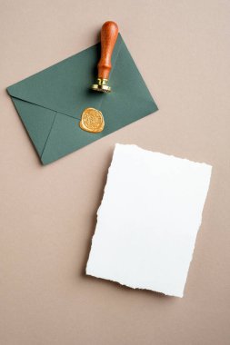 Boş kağıt kart ve pastel bej arka planda balmumu mühür damgalı yeşil zarf. Düz konum, üst görünüm, kopyalama alanı.
